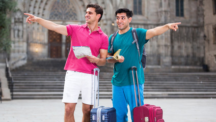 Two friends tourists with suitcases are walking with map and gui