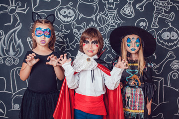 Children in scary Halloween costumes stand against a wall with drawings.