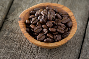 Coffee beans in wooden bowl on wooden background. Selective focus.