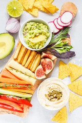 Hummus and guacamole with vegetables and snacks on a wooden board