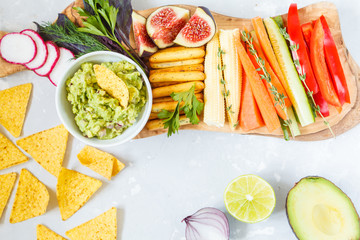 guacamole with vegetables and snacks on a wooden board