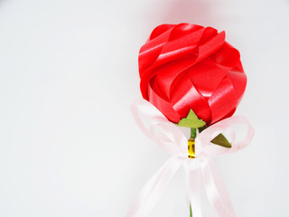 Close up handmade shiny plastic red ribbon stacked tied rose, with green stem and pink small bow thread, white background