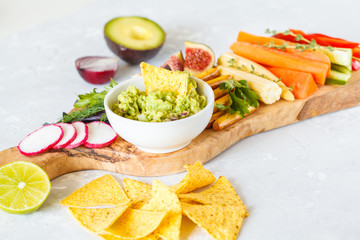 guacamole with vegetables and snacks on a wooden board
