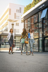 Fototapeta na wymiar Three fashionable young women strolling with shopping bags. Women walking on street.