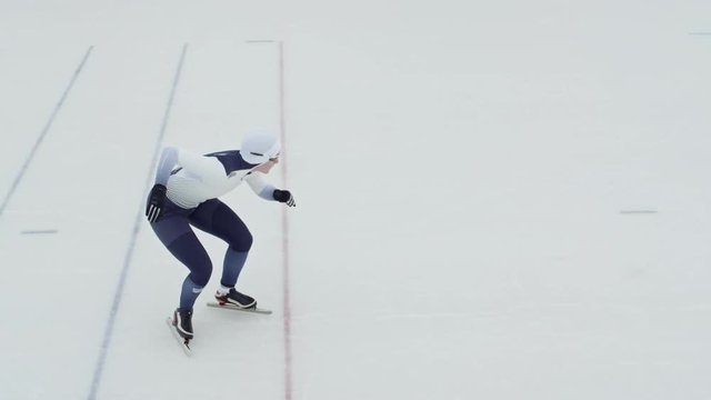 Top view with slow motion of female speed skater in spandex full-body covering suit and protective eyewear racing on ice rink
