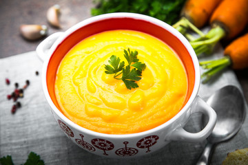 Carrot and pumpkin cream-soup on dark table.