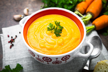 Carrot and pumpkin cream-soup on dark table.