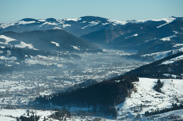 Winter landscape with mountain range at the background. Forest with mountain hill covered with white snow at the foreground.