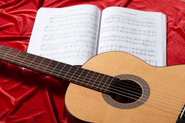 Fototapeta na wymiar acoustic guitar and music notes on red fabric, close view of objects