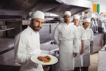 Smiling chef holding delicious dish in kitchen