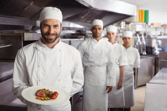 Smiling chef holding delicious dish in kitchen