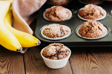 Homemade banana chocolate muffins sprinkled with sugar on a wooden background.