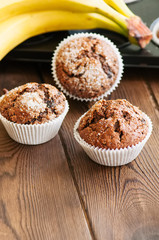 Homemade banana chocolate muffins sprinkled with sugar on a wooden background.