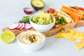 Hummus and guacamole with vegetables and snacks on a wooden board