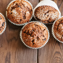 Homemade banana chocolate muffins sprinkled with sugar on a wooden background.