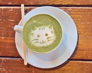 Matcha green tea latte with latte art 'Cat face' in the white cup with coffee stick on the wooden table.