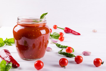 Tomato sauce, ketchup in glass jar and ingredients on a white background 