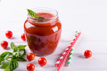 Tomato ketchup sauce with cherry tomatoes and red hot chili peppers, garlic and herbs in a  glass jar on white background. Homemade tomato sauce and fresh tomatoes