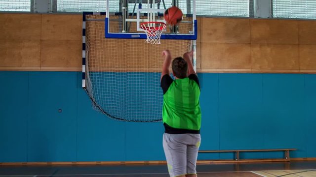 A young student misses the hoop when he is trying to throw the ball towards the rim.