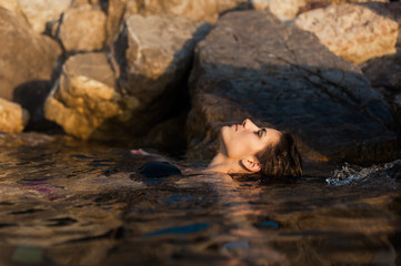 Young beautiful woman in the sea water swimming and relaxing at sunset