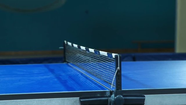 Kids are playing table tennis in a school gym. We can spot a quick game of the table tennis match and the movement of the yellow ball from one side of the table to another.