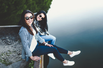 Pretty brunette girls sitting on the pier near lake