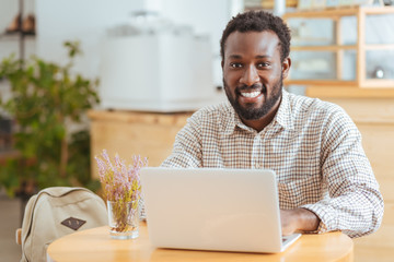 Upbeat man posing while working on laptop in cafe