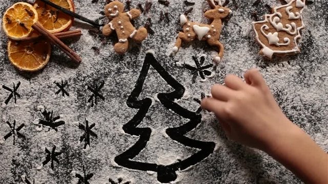 Child hands drawing stars and christmas tree in the flour prepared to make the xmas cookies