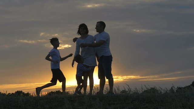 silhouette of happy family father of mother and two sons playing outdoors in field at sunset