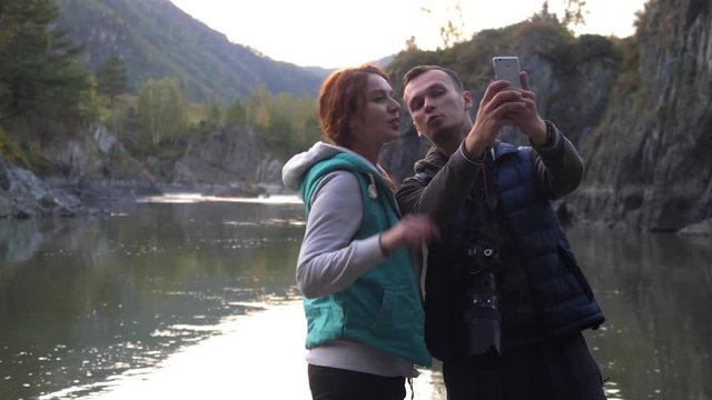 Young couple of tourists doing selfie on the background of a mountain river. Take pictures by phone. 3840x2160