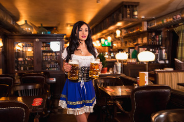 Beautiful female waitress wearing traditional dirndl and holding huge beers in a pub.