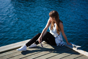 Young and happy tourist woman sitting in the harbor on wood pier