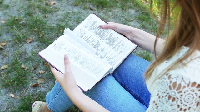4k. Girl, woman reads  Bible in  summer park  .Christian  belief team. Top view