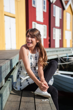 Young and happy tourist woman laing on harbor pier in Smogen town, Sweden. Beautiful traditional colorful wood houses on the background.