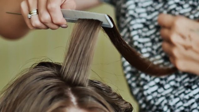 Professional hairdresser using curling iron for hair curls at salon. Hair stylist making ringlets to brunette woman. Hairdresser working with beautiful woman hair in hairdressing salon. Close up view