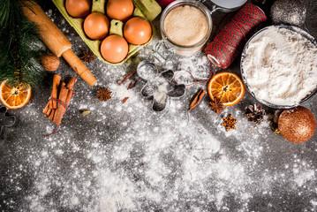 Christmas, New Year holiday cooking background. Ingredients, spices, dried oranges and baking molds, Christmas decorations (balls, fir-tree branch, cones), On black stone table, copy space top view