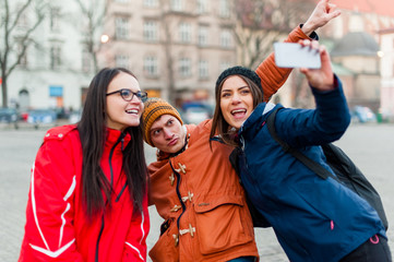 Three happy friends in a touristic city center, taking a self portrait  with wearable camera while visiting the city and having fun.