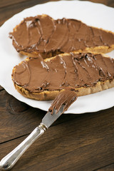 Bread with chocolate spread on brown wooden table next to a knife. Food.