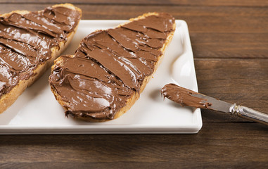 Bread with chocolate spread on brown wooden table next to a knife. Food.