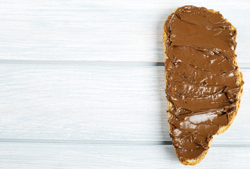 Chocolate spread on bread on wooden table. Copy space.