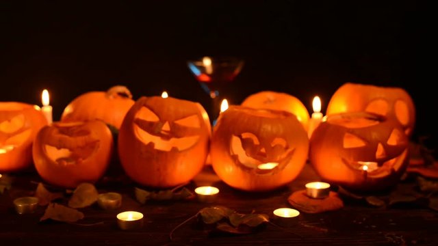 Halloween pumpkins with candles over dark background with cocktail glass, closeup, front view, rack focus