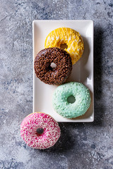 Variety of colorful glazed donuts on square plate over gray texture background. Top view with space