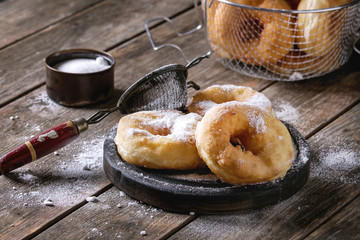 Homemade donuts with sugar powder on black serving board and in frying basket served with vintage...