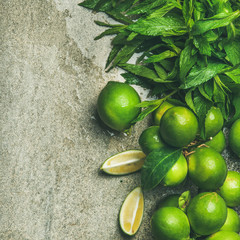 Flatlay of freshly picked organic limes and mint for making cocktail or lemonade over grey concrete stone background, top view, copy space, square crop