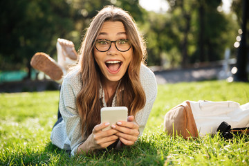 Surprised Happy brunette woman in eyeglasses lying on grass
