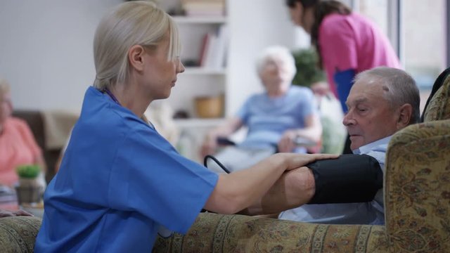 Young nurse checking elderly man's blood pressure in nursing home.