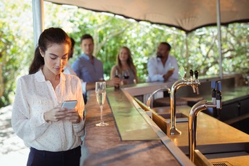 Smiling woman using mobile phone while having a glass of