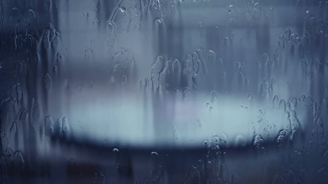 Autumn rain pouring on window, raindrops falling on glass surface viewed from the inside, handheld footage