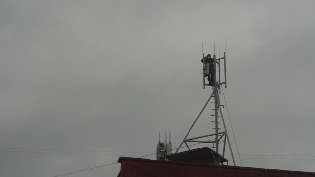 The technician serves the antennas of mobile telephony, internet, television on the background of the gray sky. The electronics engineer is dismantling the cellular aerial.
