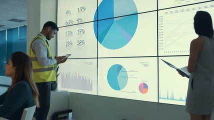  Business team looking at large video screen & computers with charts & data - Powered by Adobe